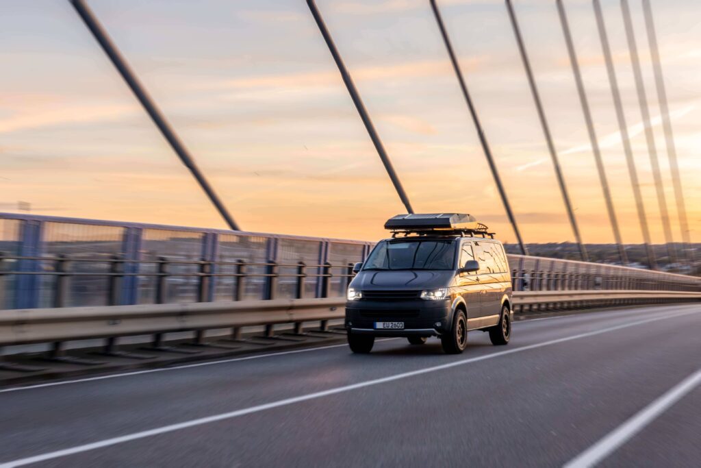 minivan with roof box driving across bridge golden hour sunset travel